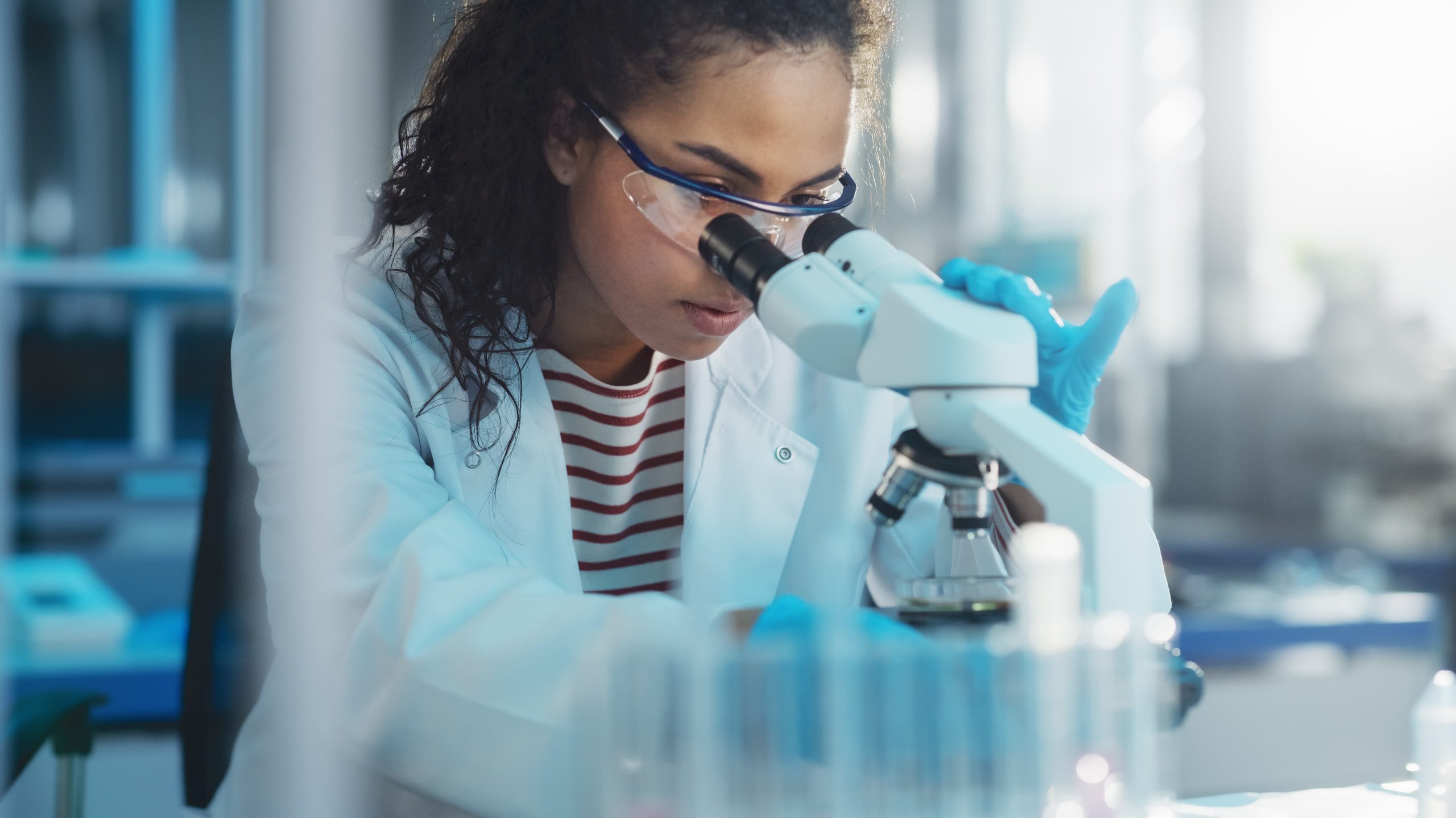 A trained biomedical technician examines a sample through a microscrope.
